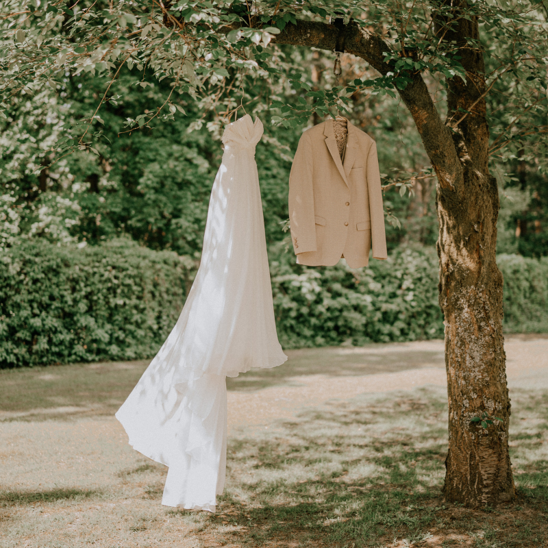 Brautkleid und Anzug hängen an einem Ast im Garten